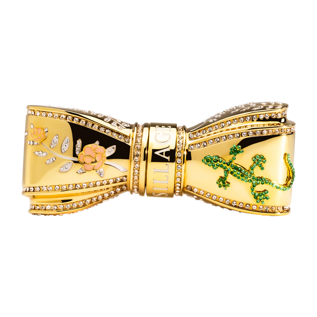 A gold bow lipstick case adorned with pink floral and gecko accents, encrusted with hand-placed Swarovski crystals.